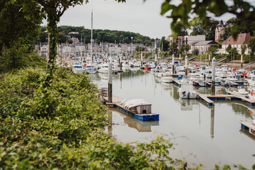Fototapeta na wymiar Yachts parking in Saint-Valery-en-Caux harbour in France. Beautiful view of the bay with yachts through the crown of trees
