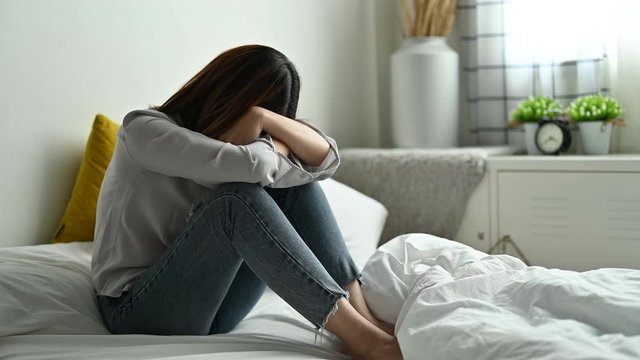 Depression and sadness concept,Young asian woman covering her face sitting on bed