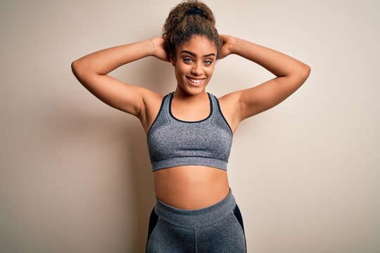 Young african american sportswoman doing sport wearing sportswear over white background relaxing and stretching, arms and hands behind head and neck smiling happy