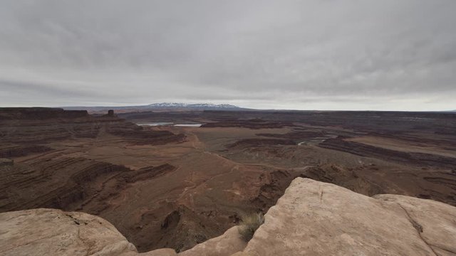 A wide timelapse looking out across Canyonlands National Park and the La Sal Mountains from Dead Horse Point as a thick layer of cloud flows overhead.