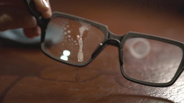 Clear Eyeglasses Cleaning By Spraying Some Water And Wiping With Blue Cloth. -closeup shot