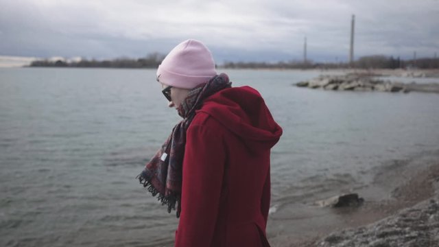 A Lonely Woman Wearing Red Winter Coat And Pink Beanie Hat Standing Near The Sea In Canada - Closeup Shot