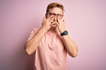 Young handsome redhead man wearing casual t-shirt standing over isolated pink background rubbing...