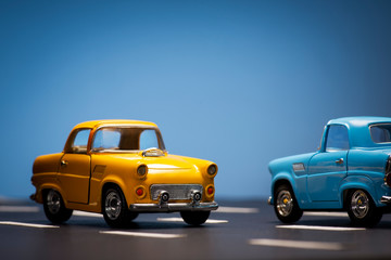 Two toy cas on a blue background and asphalt road.