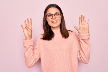 Young beautiful brunette woman wearing casual sweater and glasses over pink background showing and...