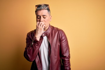 Young handsome modern man wearing fashion leather jacket and sunglasses over yellow background looking stressed and nervous with hands on mouth biting nails. Anxiety problem.