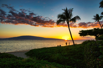Fototapeta premium Colorful sunset photo of the ocean and people silhouetted near the shore.