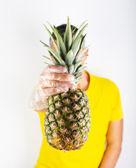 A man in yellow t-shirt wears supermarket gloves and holds ananas. Safety buying