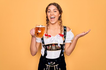 Beautiful blonde german woman with blue eyes wearing octoberfest dress drinking jar of beer very happy and excited, winner expression celebrating victory screaming with big smile and raised hands