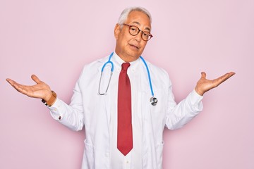 Middle age senior grey-haired doctor man wearing stethoscope and professional medical coat clueless and confused expression with arms and hands raised. Doubt concept.