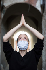 Coronavirus outbreak. Young caucasian woman wearing medical protection face mask praying over...
