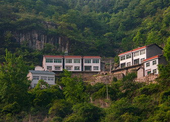 Fototapeta na wymiar Yichang, China - May 5, 2010: New white houses with red roofs built above cliff on slope of Green foliage covered mountain.