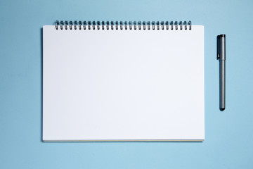 Blank spiral notebook and pen isolated on blue background
