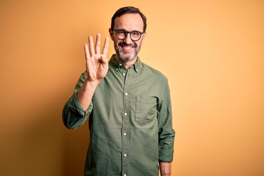 Middle age hoary man wearing casual green shirt and glasses over isolated yellow background showing and pointing up with fingers number four while smiling confident and happy.