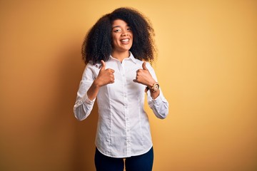 Young beautiful african american elegant woman with afro hair standing over yellow background success sign doing positive gesture with hand, thumbs up smiling and happy. Cheerful expression and winner