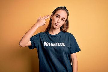 Young beautiful woman wearing volunteer t-shirt doing volunteering over yellow background Shooting...