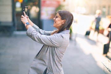 Fototapeta premium Młoda piękna kobieta uśmiechnięta szczęśliwa i pewna siebie. Stojąc z uśmiechem na twarzy, zrób selfie za pomocą smartfona w mieście