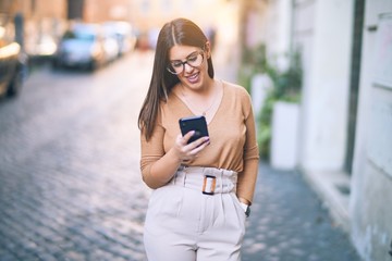 Fototapeta premium Young beautiful woman smiling happy and confident. Standing with smile on face using smartphone at the city