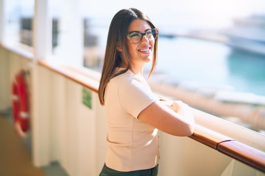 Young beautiful woman on vacation smiling happy and confident. Standing on a deck of ship with smile on face doing a cruise