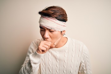 Young handsome chinese man injured for accident wearing bandage and strips on head feeling unwell and coughing as symptom for cold or bronchitis. Health care concept.