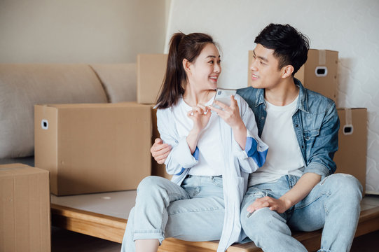 Young Asian Couple Using A Cell Phone In New Home