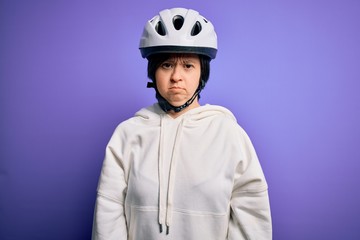 Young down syndrome cyclist woman wearing security bike helmet over purple background with serious expression on face. Simple and natural looking at the camera.