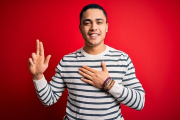 Young brazilian man wearing casual striped t-shirt standing over isolated red background smiling...