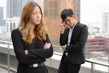 Stressed young Asian business couple looking upset together in the city