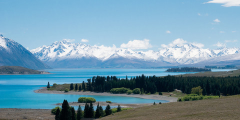 Wide vista with beautiful alpine scenery, turquoise glacier lake with snowy mountains in backdrop. Shot at Lake Tekapo, New Zealand