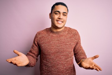 Young brazilian man wearing casual sweater standing over isolated pink background clueless and...