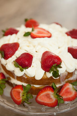 Two layer cake with strawberries and whipped cream on a glass cake platter