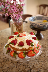 Two layer cake with strawberries and whipped cream on a glass cake platter