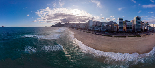 Wide panorama of near empty beach and boulevard of Ipanema in Rio de Janeiro during the COVID-19 Corona virus outbreak with dramatic clouds over the Two Brothers mountain behind [April 13, 2020]