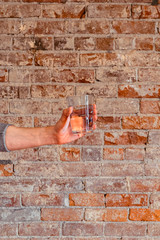 Human hand holding out a glass of water, isolated against a brick wall background