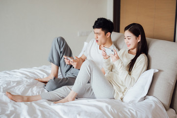 Naklejka na ściany i meble Young Asian couple at home using a smartphone
