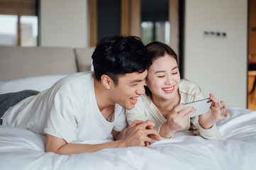 Obraz premium Young Asian couple at home using a smartphone