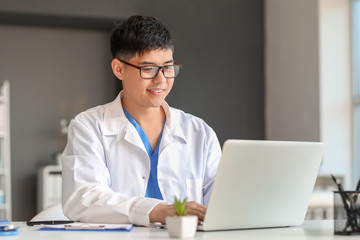 Male Asian doctor working on laptop in clinic