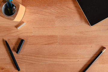 Flat Lay image of a wooden desk with writing tools and an empty space in the middle for copy