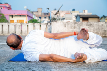Senior Citizen or an Old Indian Man Performing Yoga Early Morning, in his Terrace in white Tshirt and Pants.
Stay Home Stay Safe and Fit