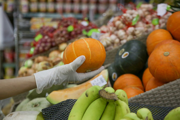 Woman wearing rubber protective gloves while grocery shopping. Close up of hands in latex gloves buying vegetables. Coronavirus outbreak protection and prevention.