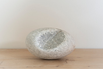 White oval pebble with a piece missing on striped pine. Smooth round stone from a beach in Skiathos.