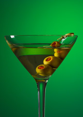 Martini and green olives on knotted bamboo skewer. Glass of extra dry vermouth martini. Alcohol cocktail. Green background. For restaurant menu.