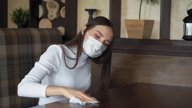 girl with long hair in a medical mask table in a cafe with a wet wipe disinfects. young woman gets infected with a coronavirus