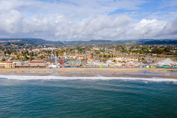 Fototapeta na wymiar Aerial drone shot of Santa Cruz Beach Boardwalk. The colorful amusement park is next to the beach with mountains in the background. 
