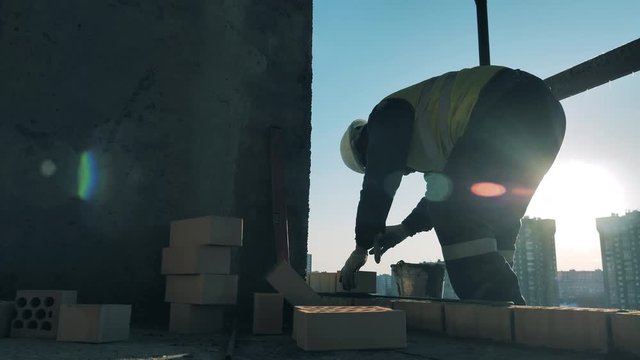 Constructor is laying bricks and fixing them in a multistory building. Construction worker at a construction site.