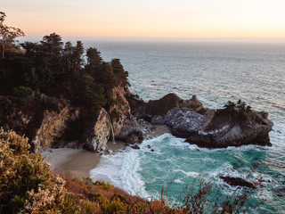 Beautiful sunset over McWay Falls in Big Sur, California. Remote waterfall on the beach with the ocean's waves crashing against the shore. 