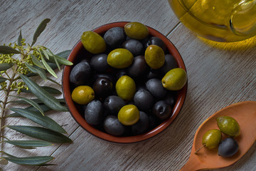 Clay bowl with black and green olives, next to olive branch and wooden spoon