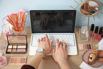 Makeup artist with cosmetics and laptop sitting at table