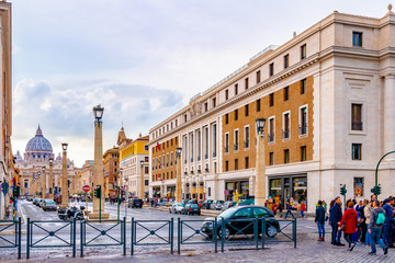 Naklejka premium Rome, Italy. People/ Tourists, vehicles/ cars, bikes/ motorbikes in Saint Peters Square in Vatican City. The Basilica Cathedral, dome shape building with cross on top, in background