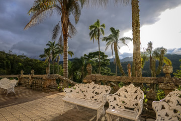Fototapeta premium View to a terrace in warm light with palm trees and a big grey cloud in the background, Caraca Natural Park, Minas Gerais, Brazil
